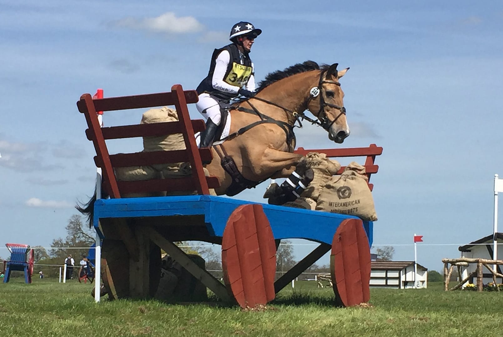A horse and rider jump over a blue and brown wooden cart at Badminton Horse Trials.